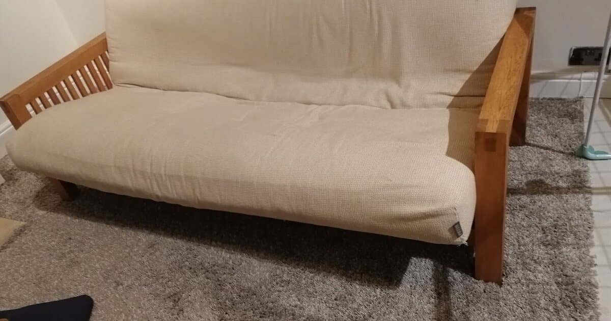 An old futon sofa with a cream cushion, ready for collection