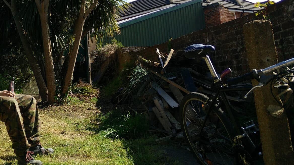 Old bicycles, timber and green waste in an overgrown garden corner