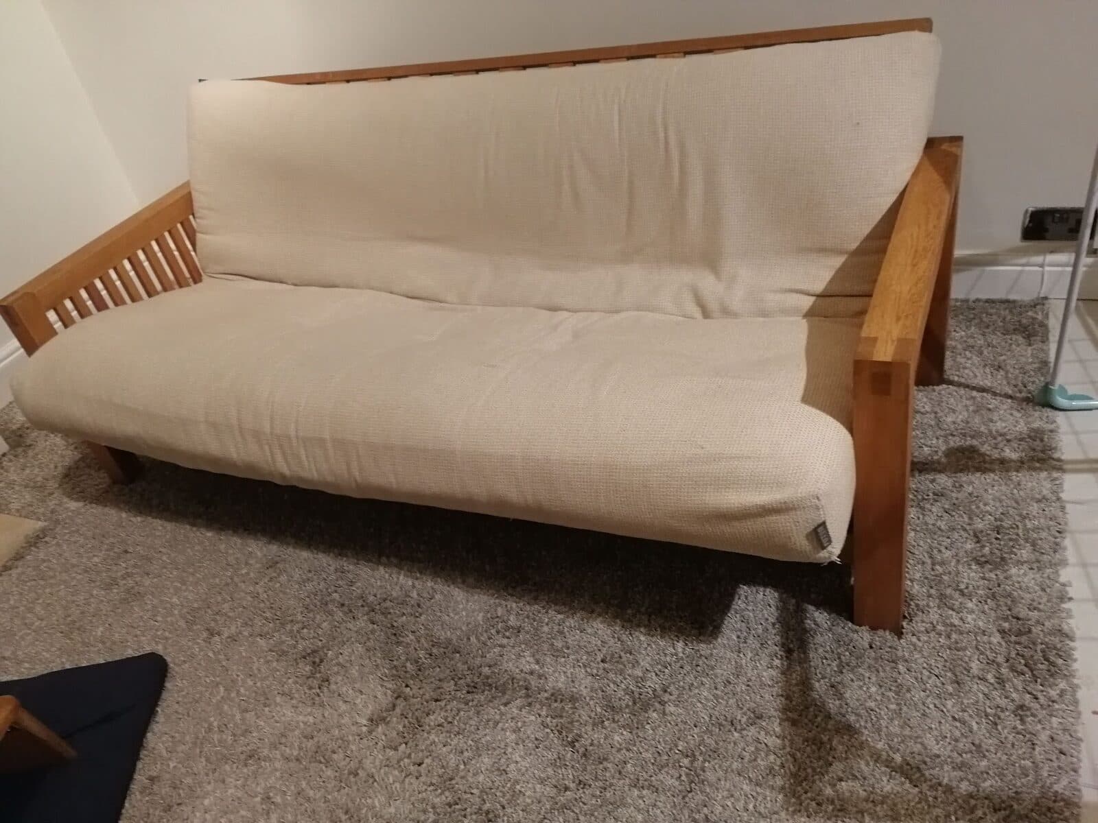 An old futon sofa with a cream cushion, ready for collection